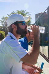 Two professional players hydrating after a hard game of tennis. They are friends and are sitting resting for the game. They are happy and laughing. 