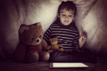 Cute little kid with his friend teddy bear using tablet computer