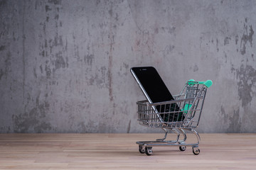 Shopping cart with smart phone inside, on the wooden table