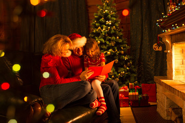 Wall Mural - Family read stories at Christmas time sitting on sofa in front of fireplace