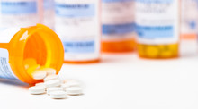 Round White Prescription Medication Medicine Pill Tablets Spilling From A Bottle With Numerous Full Bottles In Background