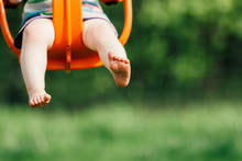Focus On Toddler Girl's Feet And Legs As She Swings In An Orange Baby Swing At A Playground