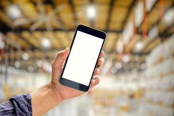 Close up of a man showing blank screen mobile smart phone at blurred warehouse or storehouse background.