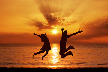 Wall Mural - Young couple in a jump on the sea beach at sunset