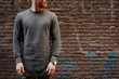 A cropped photo of a bearded hipster guy wearing blankl gray long sleeve t-shirt while standing on a brick wall background on a street. Empty place for you logo or design.