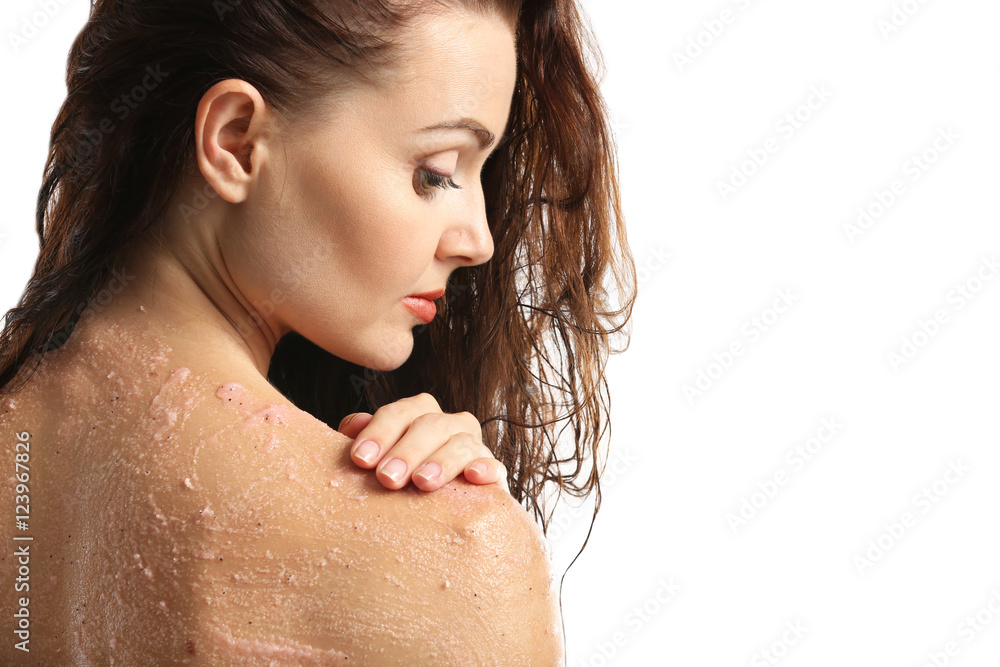 Young woman applying scrub on shoulder on white background