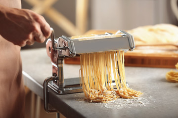 Wall Mural - Man using pasta machine to prepare spaghetti, close up view