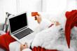 © Africa Studio - Santa Claus with credit card and laptop on couch at home