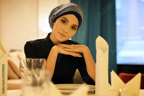 Photo portrait of a beautiful Muslim woman sitting at a table in a restaurant and look