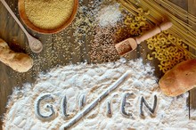Gluten Free Cereals Corn, Rice, Buckwheat, Quinoa, Millet, Pasta And Flour With Scratched Text Gluten On Brown Wooden Background