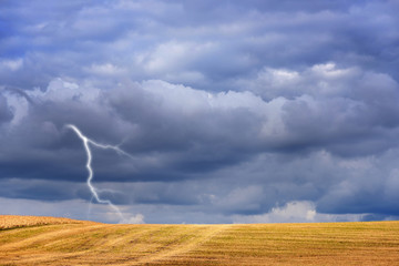 Dark storm clouds and lightning above autumn fields after harvesting