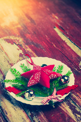 Wall Mural - Holiday decorations red star textile Christmas tree on a white plate, jingle bells, fir branches on red wooden background. Christmas background, New year.