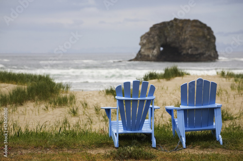 Two Blue Adirondack Chairs On A Grassy Beach With Rock