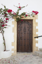 Wooden Door On A White Building With A Blossoming Vine Growing On The Wall; Vejer De La Frontera, Andalusia, Spain