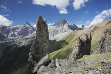 Large Rock Sentinels On Mountain Ridge With A Mountain Range And Valley In The Background With Blue Sky And Clouds; Alberta, Canada