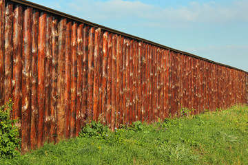 Wall Mural - Long wooden fence made of oak tree trunks on green grass