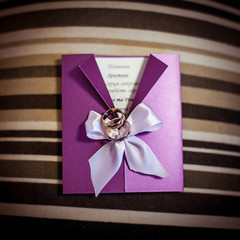 Wedding rings lie on the violet invitation letter