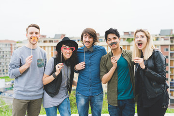 Wall Mural - Knee figure of group of young multiethnic friends posing using masks in shape of object - funny, happiness, having fun concept