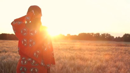 Wall Mural - African woman in traditional clothes standing in a field of crops at sunset or sunrise