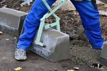 Worker Lifts Concrete Curb With A Manual Lifting Tool. Concrete Kerb Installation At Sidewalk Edging.