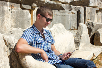 traveller using his cellphone sitting on the ruins of amphitheat