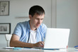 © fizkes - Portrait of a young man working at the desk with a laptop, looking at the screen, education, business concept photo