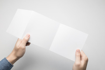 Man in blue t-shirt is holding a square Z-Fold white paper flyer