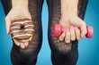 Woman with dumbbell and donut in the hands of