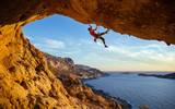 Fototapeta  - Male climber on overhanging rock against beautiful view of coast below 