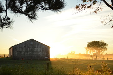 Sunrise behind a barn on a foggy morning