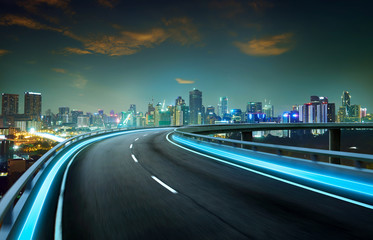 Wall Mural - Blue neon light highway overpass motion blur with city  skyline background , night scene .