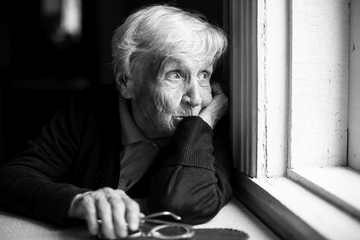 An elderly woman sadly looking out the window, a black-and-white photo.