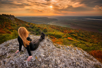 Wall Mural - sunset from the top / a woman on the top of a rock enjoys the view of sunset over an autumn forest