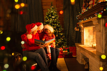 Wall Mural - Family read stories sitting on coach in front of fireplace in Christmas decorated house interior