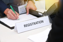 Close-up Of Registration Desk In Front Of Conference Center With Businessman Writing On The Table