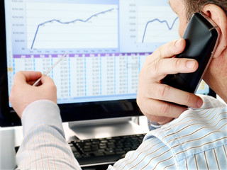 Fototapete - Man on a Phone Analyzing Financial Data and Charts on Computer Screen