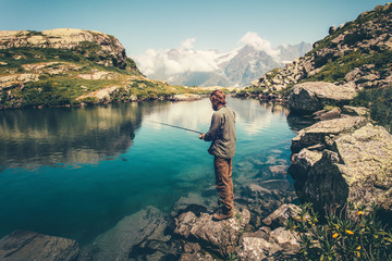 Wall Mural - Young Man fishing on Lake with rod mountains landscape on background Travel Lifestyle concept summer vacations