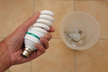 Holding A Low Energy CFL Light Bulb With Discarded Tungsten Bulbs In Background