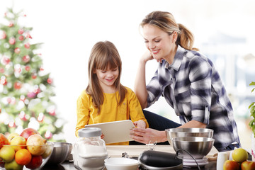 Wall Mural - Christmas time. Portrait of cute daughter and her mom baking christmas cookies together in the kitchen.