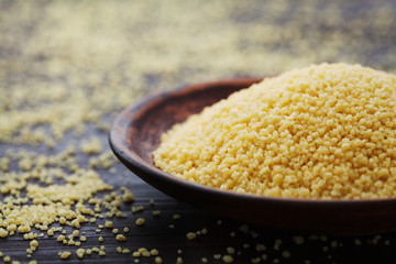 Raw couscous in bowl on dark rustic background