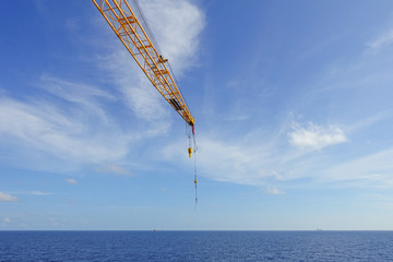 Crane boom and crane hook in the sea with sky and clouds backgro