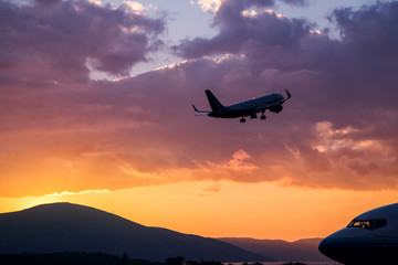 Wall Mural - Airplane flying at purple sunset over mountains and sea
