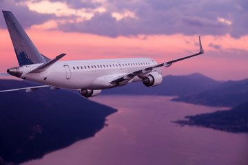 Wall Mural - Airplane flying at purple sunset over mountains and sea