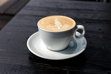 A white cup of cappuccino on the dark wooden table