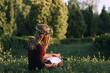 © golubovy - Attractive woman in wreath reading at nature, back view, copy space. Young blonde sitting with book in blooming meadow. Summer, relax, freshness, loneliness concept