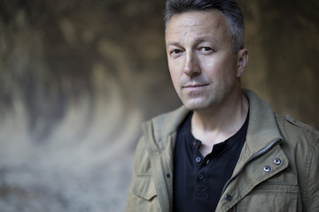 Outdoor male portrait. Man standing near rock wall and looking u