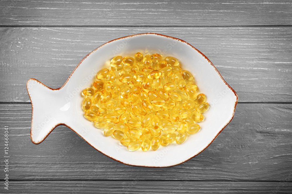 Cod liver oil capsules in fish shaped saucer on wooden background