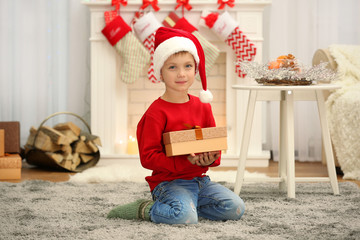 Wall Mural - Cute little boy in Santa hat with Christmas present at home