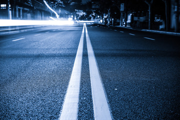 Nights lights of the big city, the night avenue with road markings and headlights of the approaching cars, close up view from asphalt level.