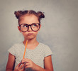Thinking grimacing kid girl in glasses looking and holding penci